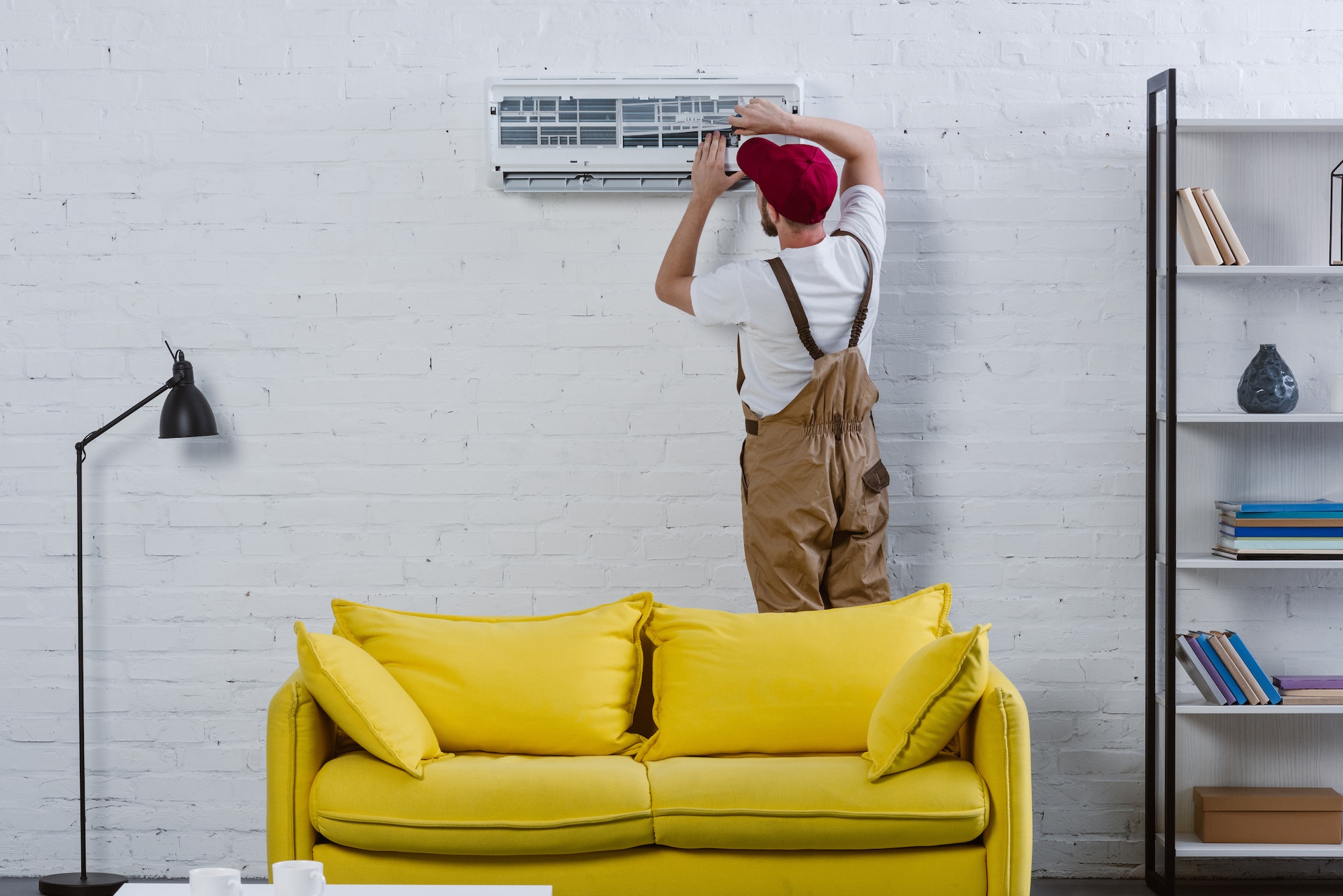 professional repairman fixing air conditioner hanging on white brick wall
